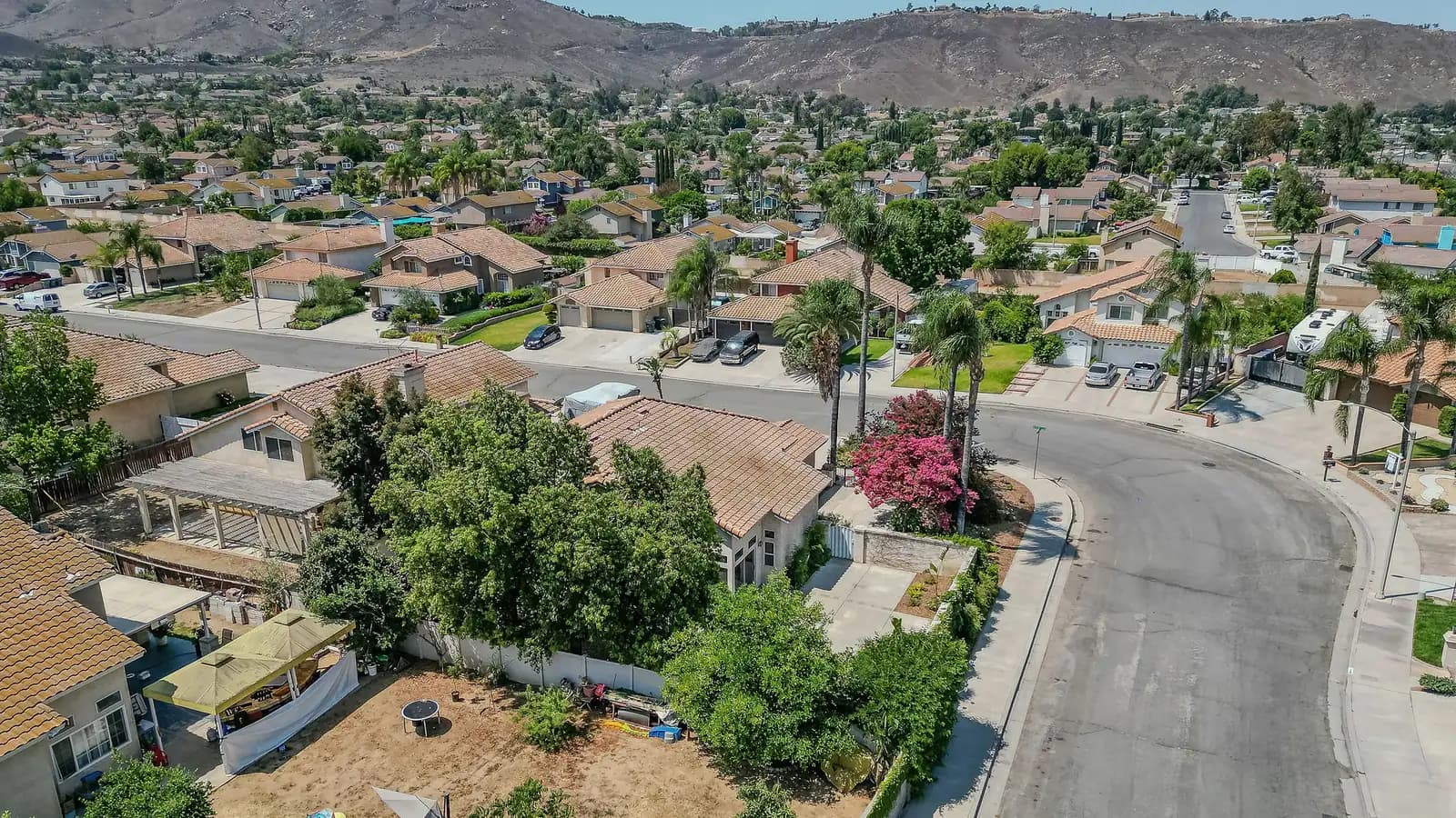 Aerial view of a Riverside, California neighborhood of single-family homes with tile roofs, with dry hills rising behind.